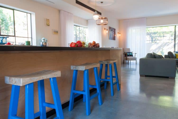 בית פרטי בהרצליה עם רצפת בטון מוחלק, פרופיל בלגי בחלונות ,כיסאות עץ מלא עם רגלי עץ צבועות בכחול , ואי עבודה במטבח עשוי עץ סנדוויץ' ליבנה