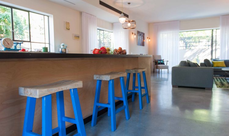 בית פרטי בהרצליה עם רצפת בטון מוחלק, פרופיל בלגי בחלונות ,כיסאות עץ מלא עם רגלי עץ צבועות בכחול , ואי עבודה במטבח עשוי עץ סנדוויץ' ליבנה